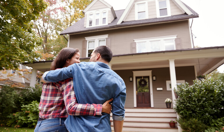 Couple standing in front of their new home.